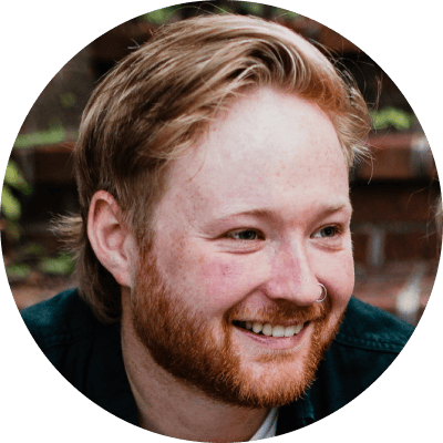 A man with a beard smiling in front of a brick wall.