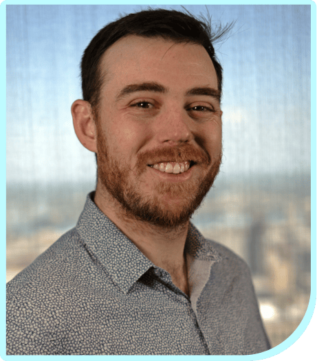 A man with a beard smiling in front of a city.
